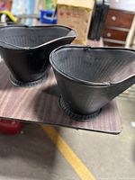 Pair of black metal coal buckets sitting on a table, showing overall shape and exterior features