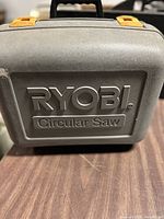 Closed Ryobi branded hard plastic carrying case for circular saw, grey with yellow latches.