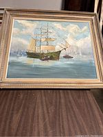 Front view of the framed ship painting showing a large sailing ship on calm water with other boats and a cloudy sky.