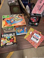 Photo of vintage Pop-Up Pinball game, Trouble board game, small toy car in box, and Wheres Waldo books displayed on table.
