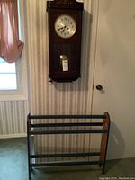 Image showing the mahogany pendulum wall clock mounted on wall above the pine painted blanket rack in front of striped wallpaper.