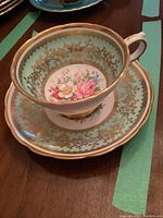 Side view of the teacup sitting inside the saucer showing floral pattern and gold scroll design on turquoise background.