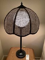 Full view of the table lamp turned on, showing the metal base and cane woven shade glowing with light.