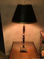 Full view of the ornate table lamp with shade on a wooden table against wallpaper.