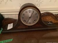 Full view of the Sessions mantel clock on a wooden surface showing its curved wooden case and round clock face.