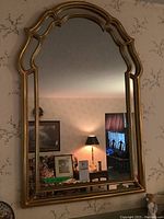 Full frontal view of the gilded finish wall mirror showing the reflective quality and ornate top edge.