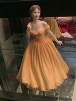 Front and three-quarter view of Royal Doulton Elizabeth figurine wearing a yellow gown with off-shoulder sleeves, holding a small flower.