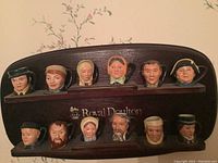 Front view of twelve Royal Doulton Toby miniature character mugs arranged on the custom wooden rack with two shelves showing detailed character faces and the Royal Doulton inscription on the rack.