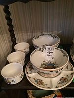 Photo showing the full set including large bowl, several small bowls, divided canapé plate, and small bakers arranged on a wooden shelf.