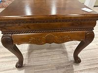 Close-up of the table's carved leg and apron showing decorative leaf and shell details.