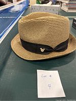 Side view of light brown woven fedora with black band and Mickey Mouse pin