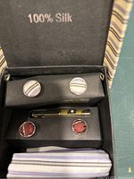Box containing two pairs of cufflinks, one tie clip, and a folded silk pocket square inside a box labeled 100% Silk.