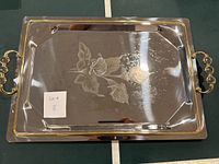 Full view of rectangular metal tray with gold-tone handles and engraved floral design in center.
