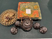 Photo showing complete set including tea pot, four cups, four plates, and a metal plate holding small forks and spoons.