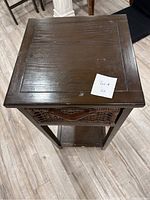 Top view of wooden side table showing square wood tabletop with scratches and a small tag labeled 'Lot 4'.
