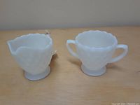 Two piece set of white milk glass creamer and sugar bowl with bubble texture pattern, two handles on sugar bowl and spout on creamer.