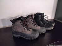 Both pairs of boots side by side on a black surface against a white wall