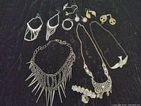 Photo showing a collection of various modern costume jewelry including spikey choker, chandelier earrings, silver hoops, leaf earrings, tree of life earrings, white crystal earrings, and a bird in flight necklace.