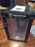 Front view of black Monster Energy mini fridge with clear door and logo.