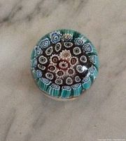 Top-down view showing the millefiori floral pattern inside the paperweight, highlighting the intricate flower designs in blue, white, brown, and turquoise.