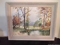 Full view of the framed oil painting depicting trees and pond landscape.