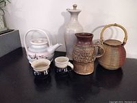 Full view of the five pottery items including two teapots, two mugs, and a vase showing different styles and glazes.