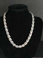 Full length view of the silver tone D’Orlan marcasite necklace on black display bust showing linked leaf-shaped segments.