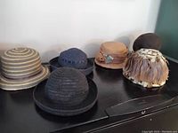 Six vintage hats displayed on a dark surface, including straw hats and feather hat, showing full lot composition.