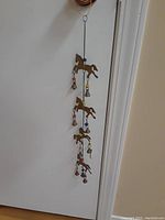 Full view of the vintage mobile hanging on a wall showing four brown metal horses with small bells attached and colorful beads.