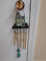 Front view of resin house wind chime showing detailed house model and metal chime tubes.