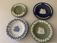 Four Jasperware pieces: two oval ashtrays (green and dark blue) and two round pin dishes with leaf decorative rims in blue and green.