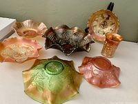 Seven pieces of vintage carnival glass laid out showing variety of marigold and green opalescent colors and patterns.
