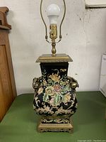 Full view of the large porcelain and brass table lamp with floral paintwork and side brass handles.