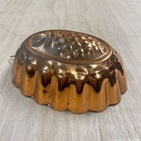 Side angle view of copper baking mold showing detailed pineapple pattern and scalloped edges