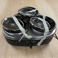 Front view of Crock-Pot sauce warming appliance with three round warming pots taped down and control knob in center.