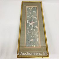 Full view of framed woven fabric panel showing birds, butterflies, and floral patterns on blue-gray background inside gold-tone frame.