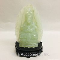 Front view of the light green translucent jade seated Buddha deity figure on a dark wooden stand, showing detailed carving and polished finish.