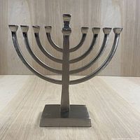 Front view of the metal menorah showing its nine candle holders and square base.