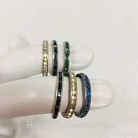 Six sterling silver rings with colored stones set in a channel setting displayed on hand mannequin fingers. Stones include blue, green, and cream colors.