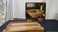 Wooden serving tray with metal handles in front of the bamboo serving bowl and utensil set box.