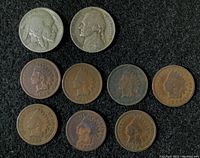 Top view of nine coins including one Buffalo Nickel (1935), one Jefferson Nickel (1946), and seven Indian Head Pennies with dates visible from 1889 to 1912, laid out on a flat surface.