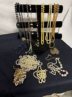 Photo showing multiple vintage costume jewelry necklaces including pearl-style beads, chains in silver and gold tones arranged on a necklace display and flat on surface.