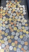 Top-down view of a broad assortment of foreign coins arranged loosely on a dark surface showing varied sizes and metallic colors.