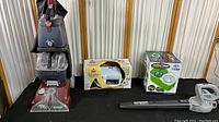 Four cleaning machines boxed and unboxed: Hoover Power Scrub Deluxe, Bissell SpotLifter, Insta Mop, Sun Joe blower.