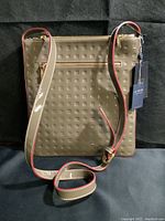 Front view of Arcadia patent leather crossbody handbag in acacia color with embossed logo pattern and zipper pocket.