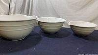 Photo showing all three white mixing bowls arranged left to right by size from largest to smallest, set on a dark cloth background against a white backdrop.