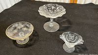 Three vintage frosted glass footed dishes displayed on black surface, showing size and design variations.