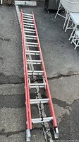 Full length view of red Werner fiberglass extension ladder on pavement, showing overall condition and metal rungs.