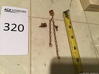 Overall view of stickpin, chain, and two charms laid out next to measuring tape