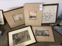 Five framed prints and photograph arranged on floor against wall